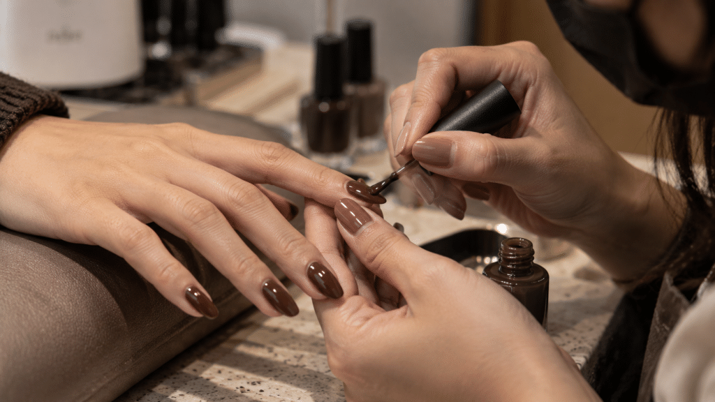 Proses presisi pengolesan lapisan cat kuku kuas halus pada chocolate brown nail art.